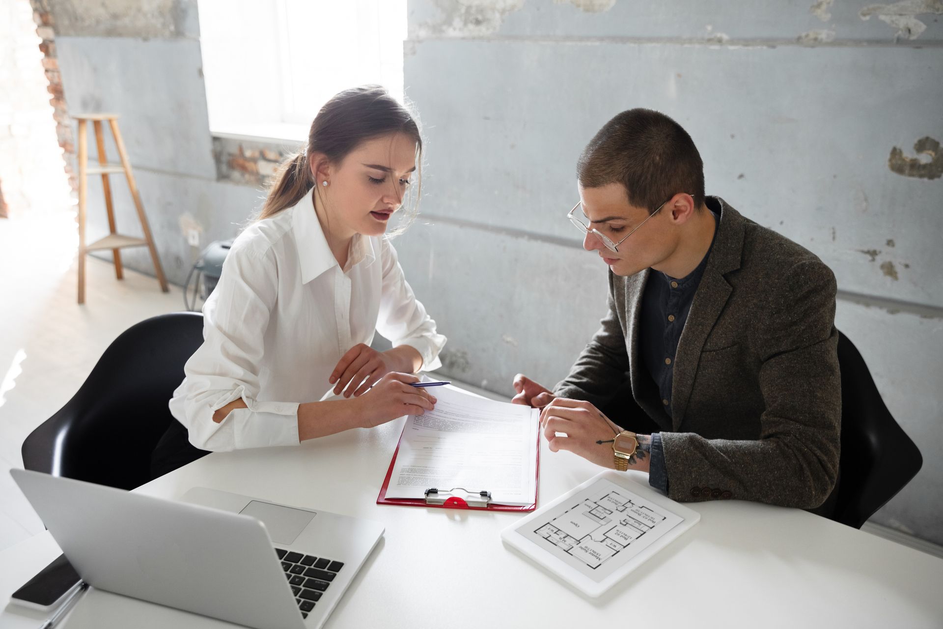A man and a woman are sitting at a table looking at a clipboard.