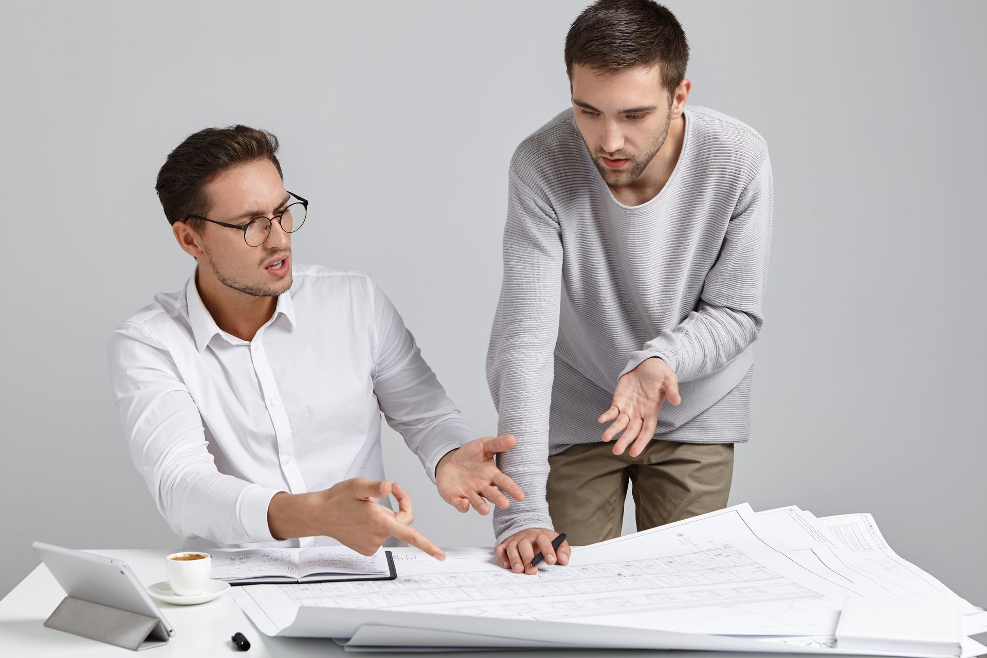 Two men are standing next to each other at a table looking at a blueprint.