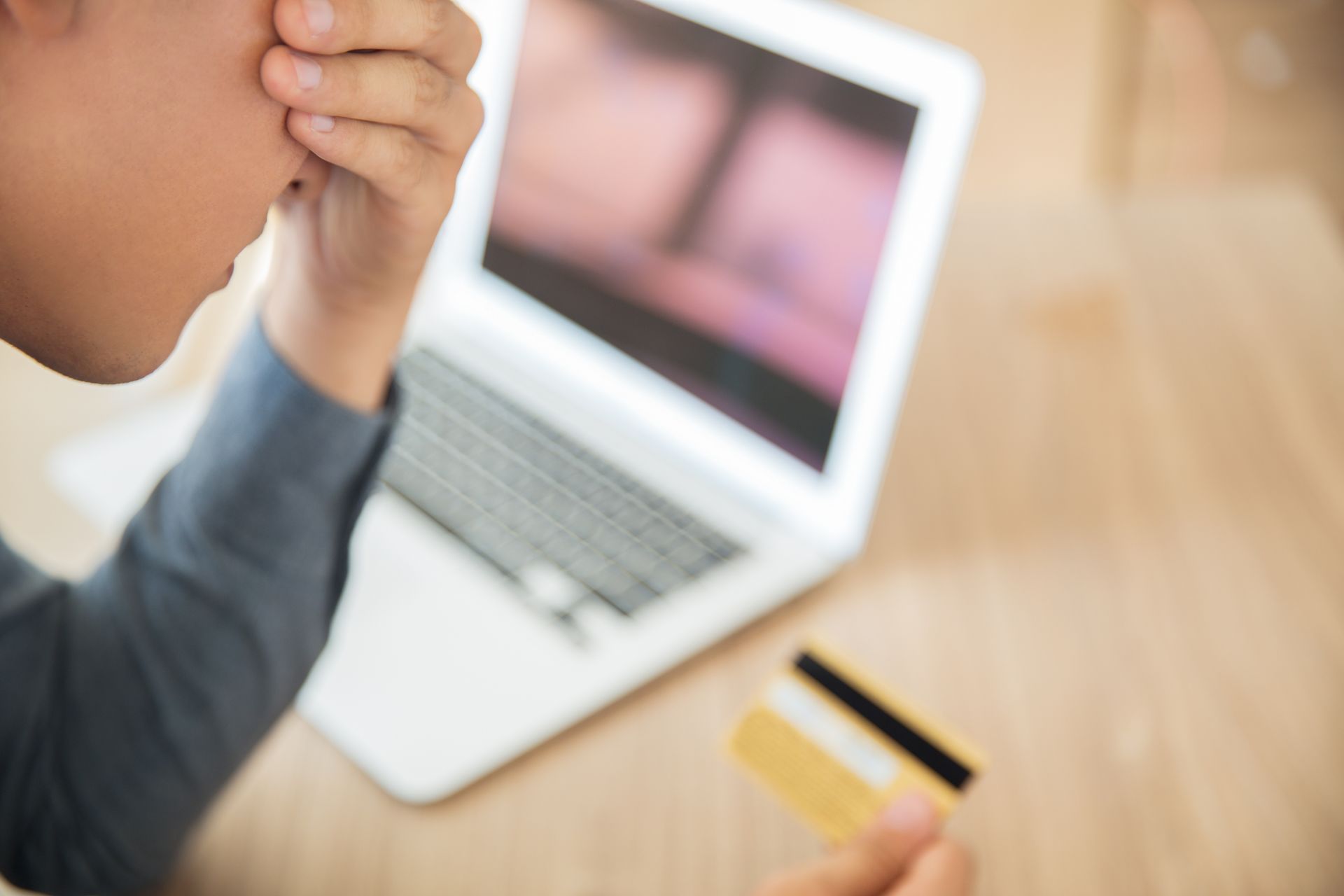 A man is holding a credit card in front of a laptop computer.