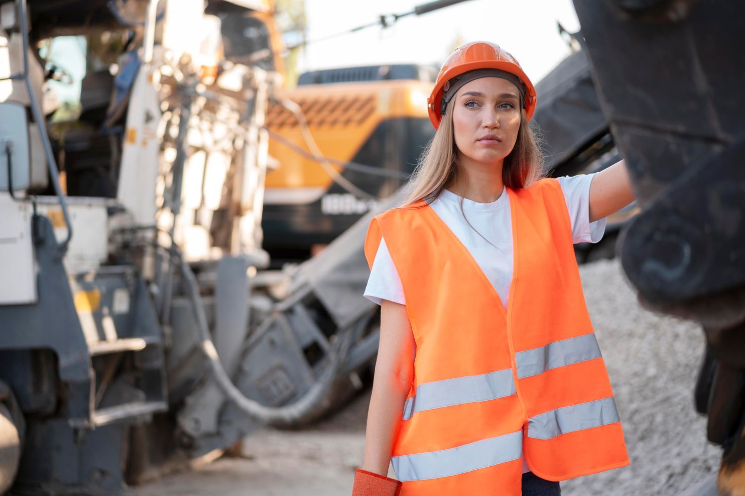 A woman in an orange vest and hard hat is standing in front of a construction site.