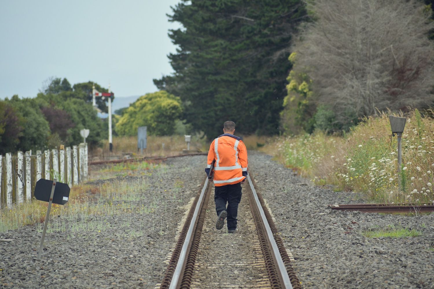 A man in an orange vest is walking down train tracks.