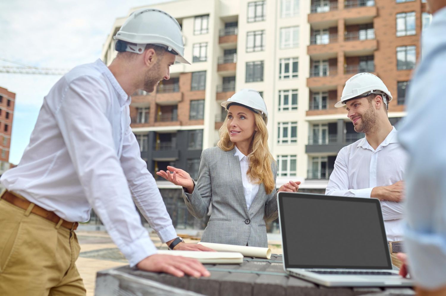 A group of construction workers are standing around a laptop computer on a construction site.