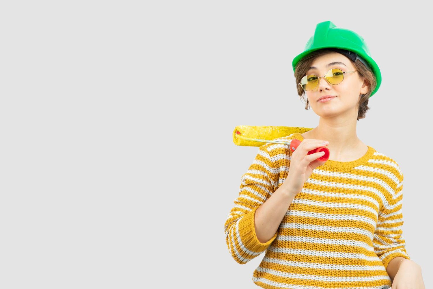 A woman wearing a hard hat and sunglasses is holding a tape measure.