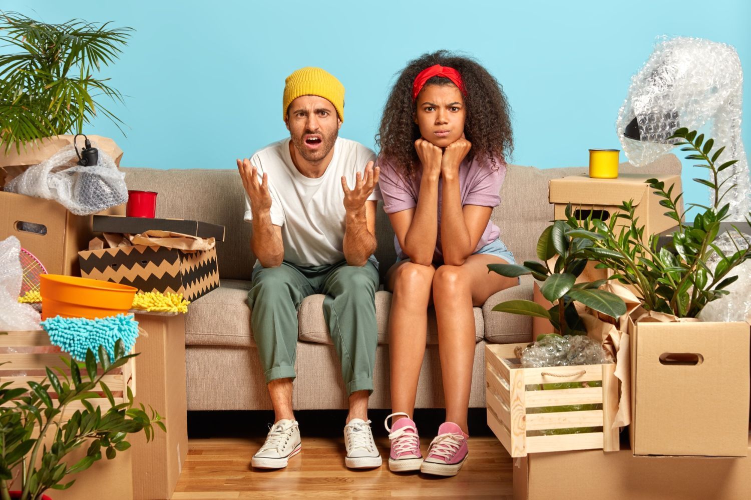 A man and a woman are sitting on a couch surrounded by cardboard boxes.