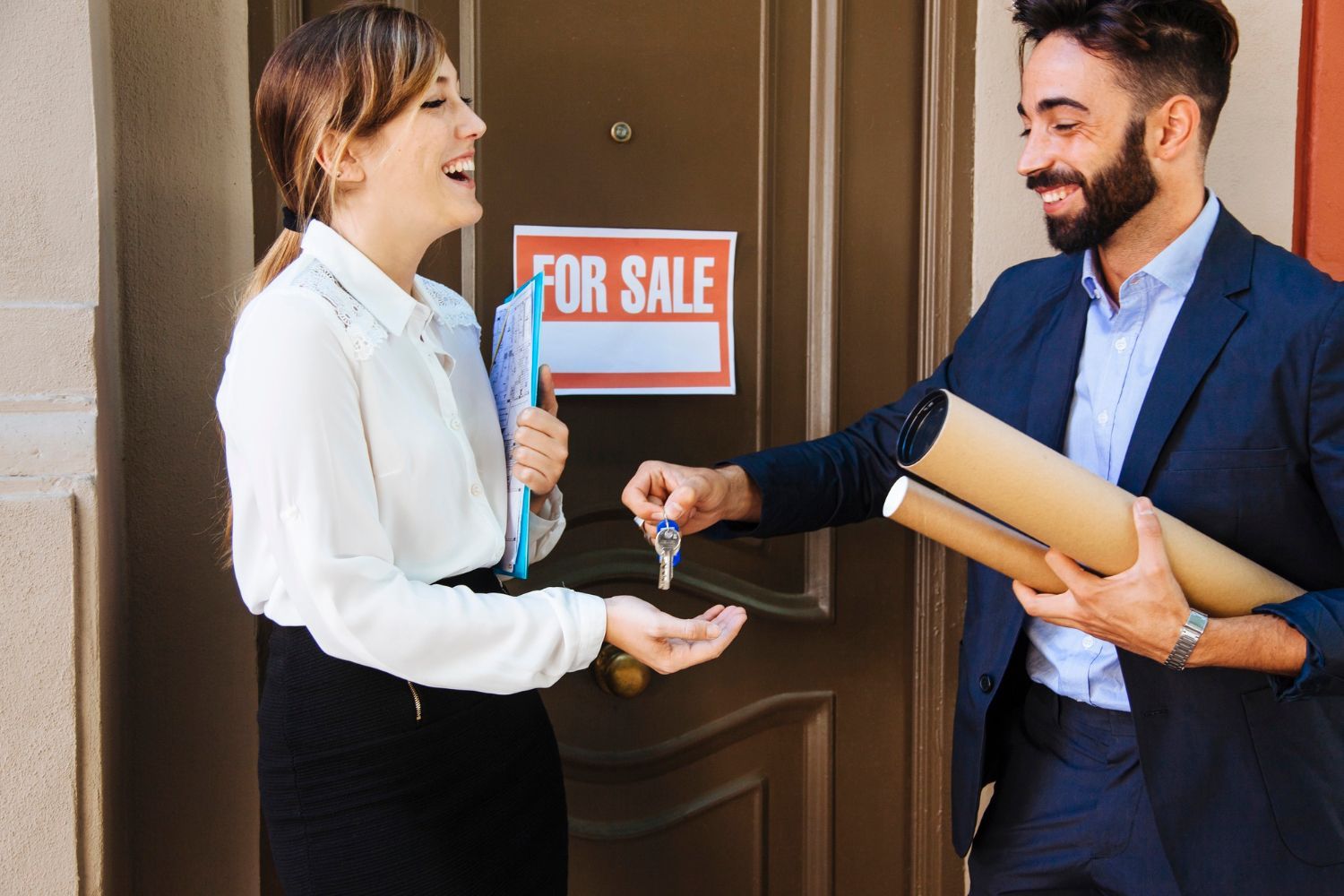 A man is giving a woman a set of keys in front of a for sale sign.