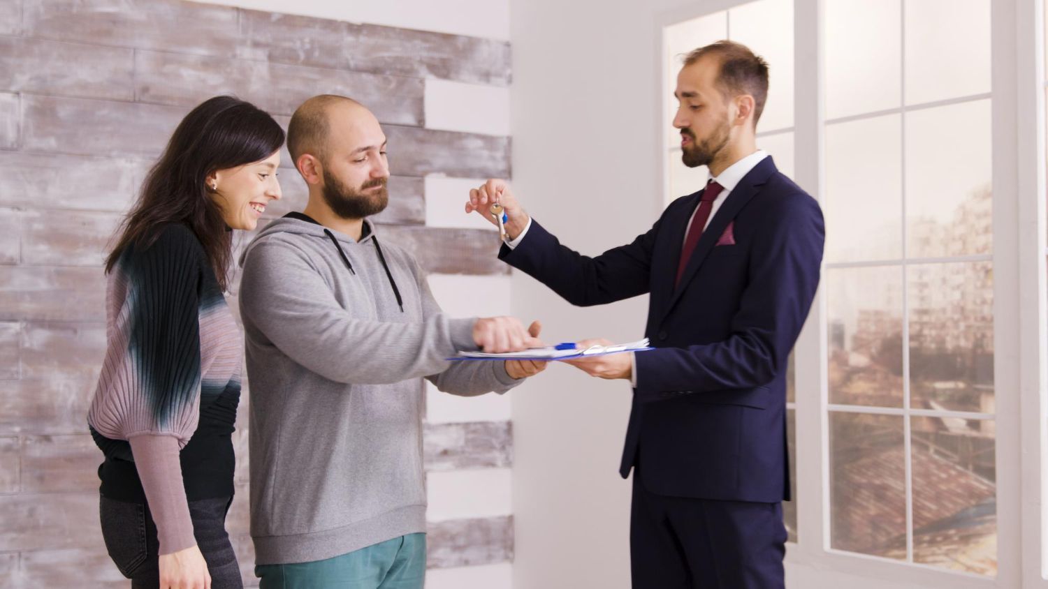 A man in a suit is giving a key to a man and woman.