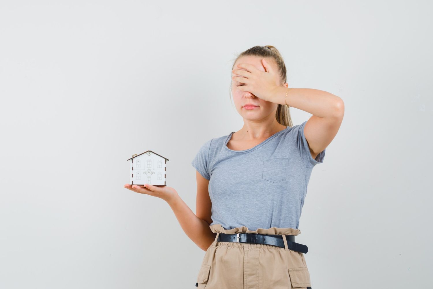 A woman is covering her face while holding a small house model.