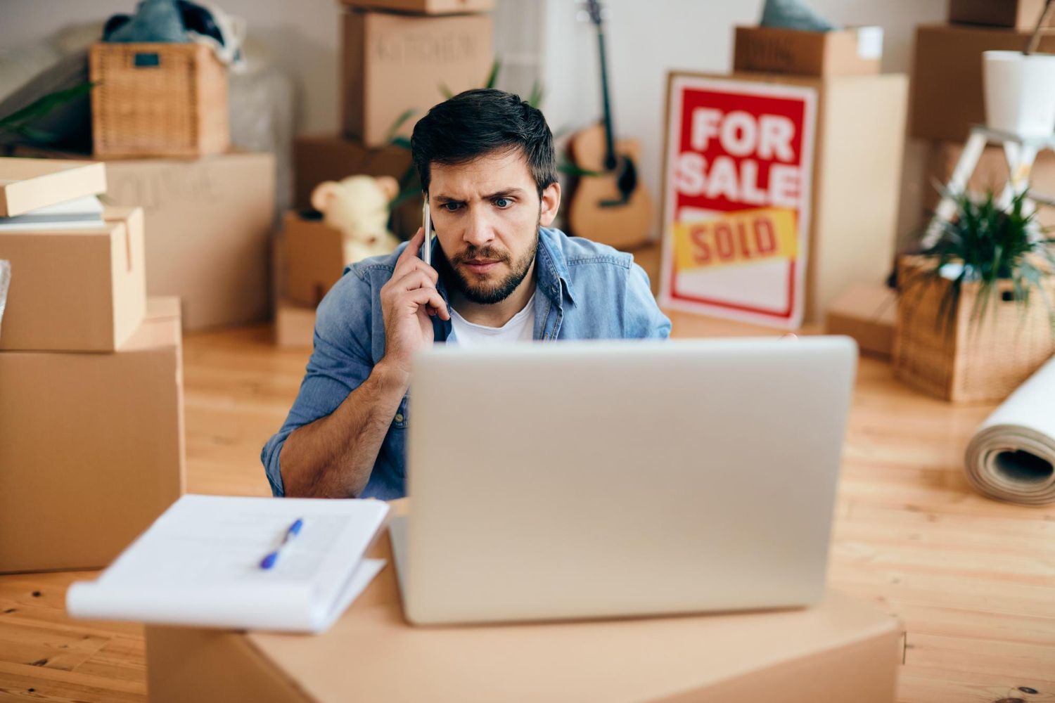 A man is sitting in front of a laptop computer talking on a cell phone.