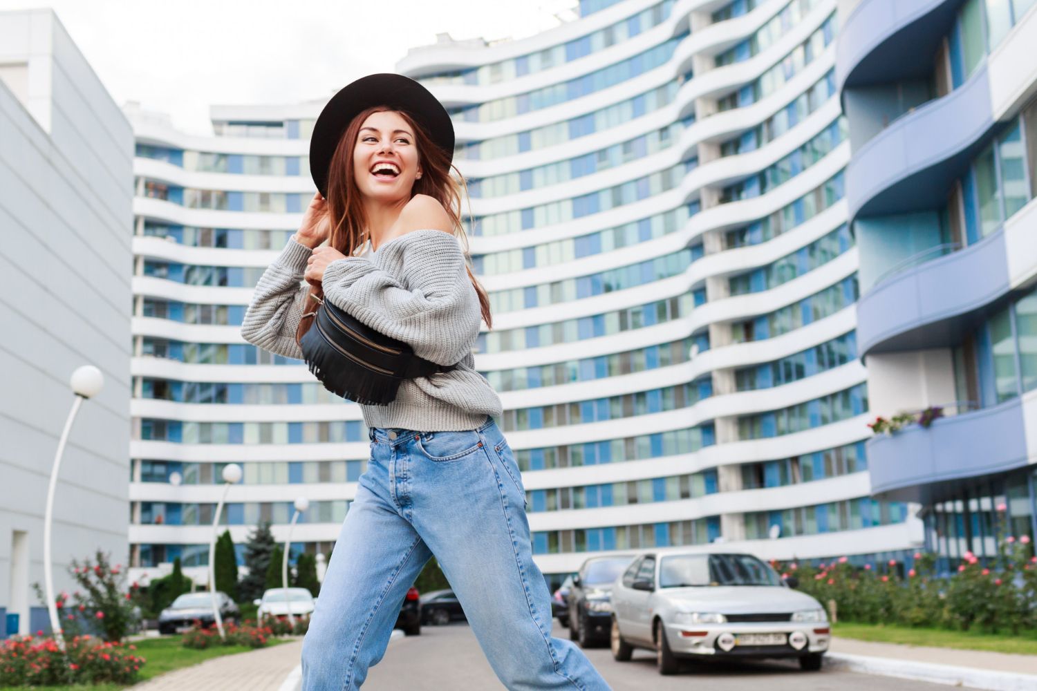 A woman in a hat and jeans is standing in front of a building.