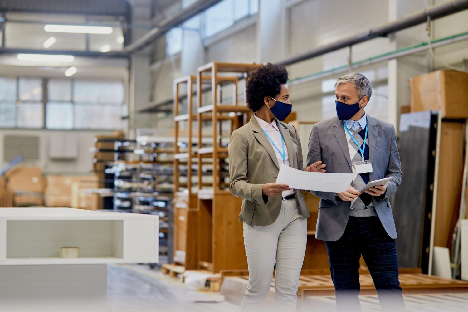 A man and a woman wearing face masks are looking at a piece of paper in a factory.