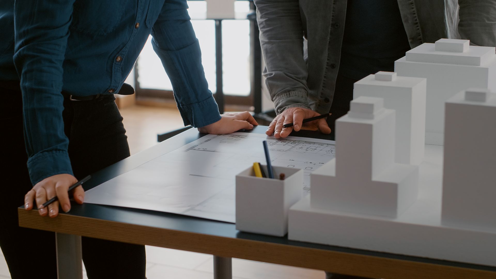 Two men are looking at a model of a building on a table.