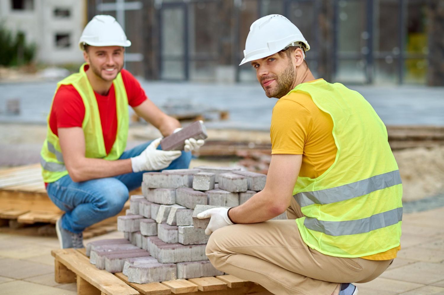 Two construction workers are working on a pallet of bricks on a construction site.