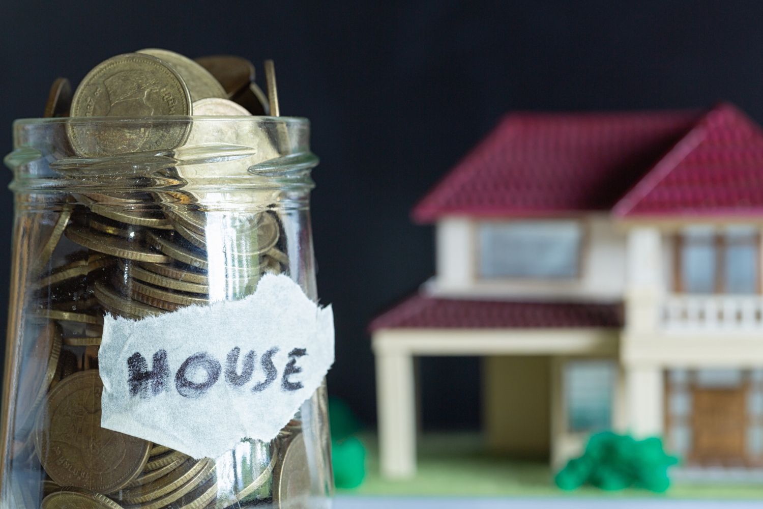 A jar filled with coins next to a model house.