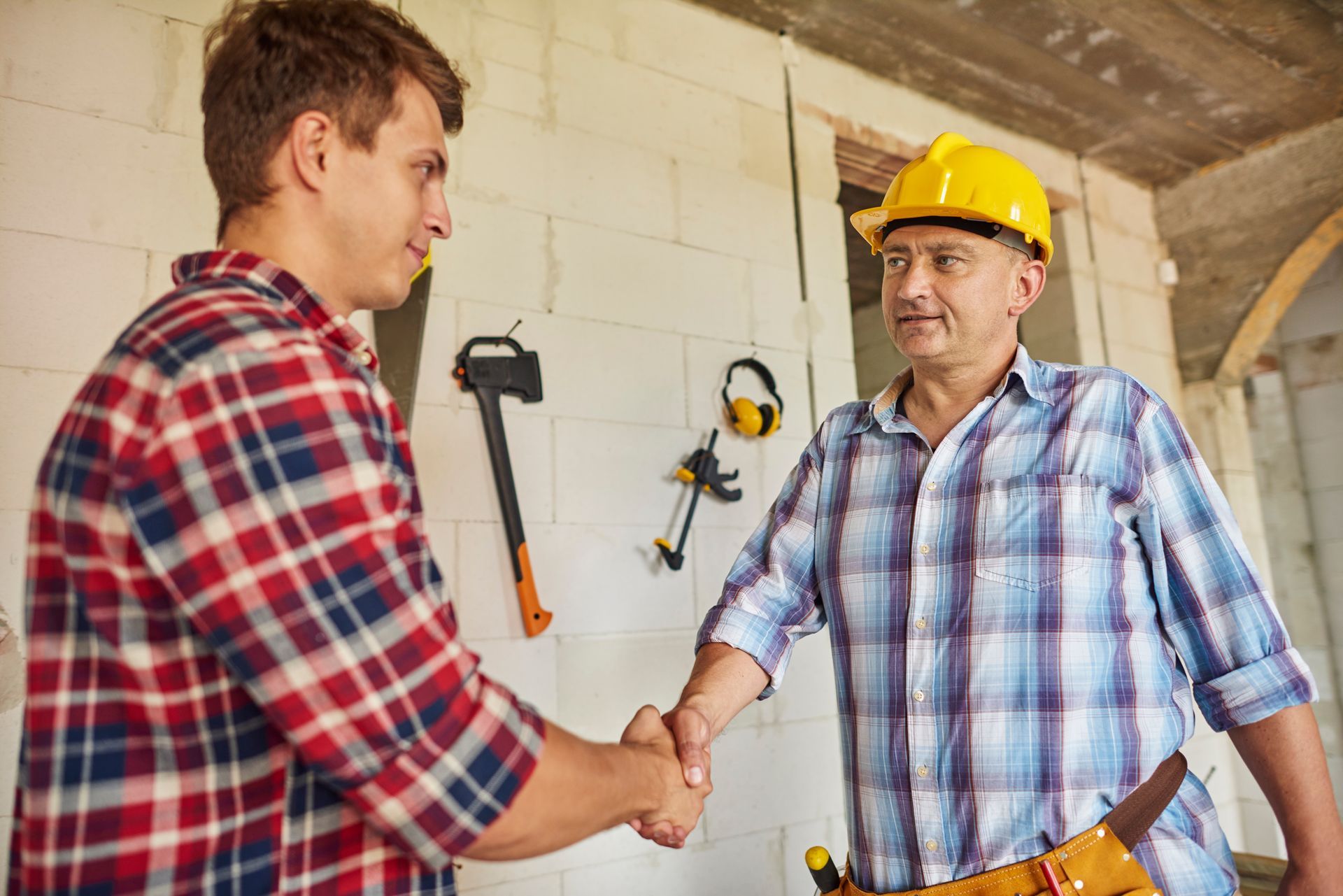 A man in a hard hat is shaking hands with another man in a plaid shirt.