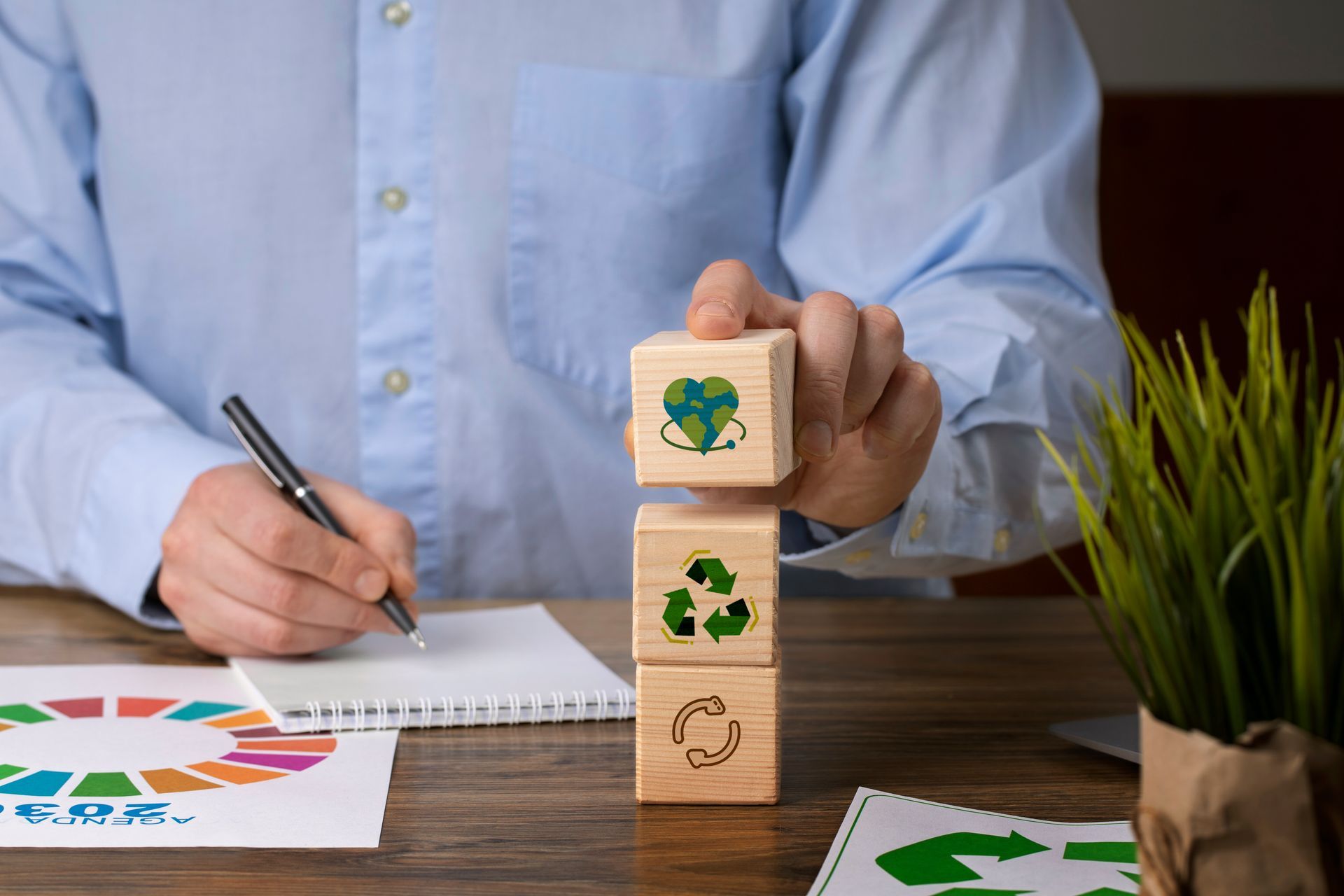 A man is sitting at a desk stacking wooden blocks with recycling symbols on them.