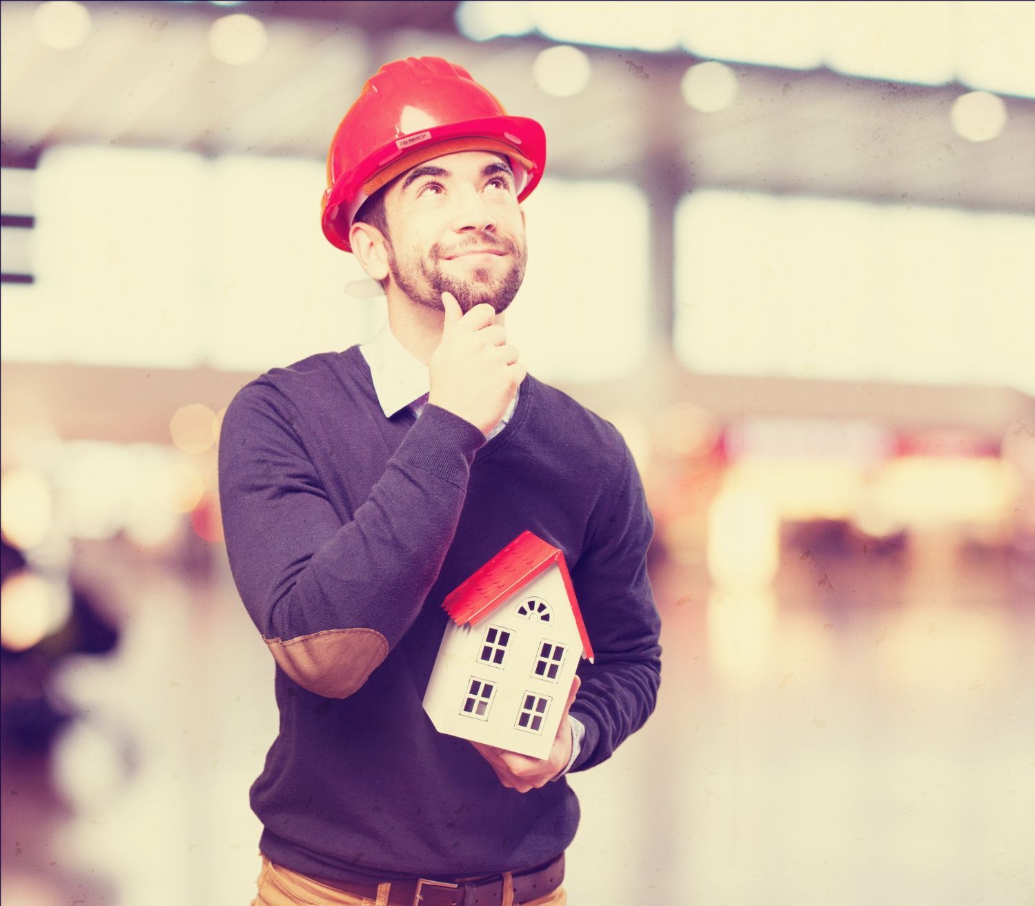 A man wearing a hard hat is holding a model house.