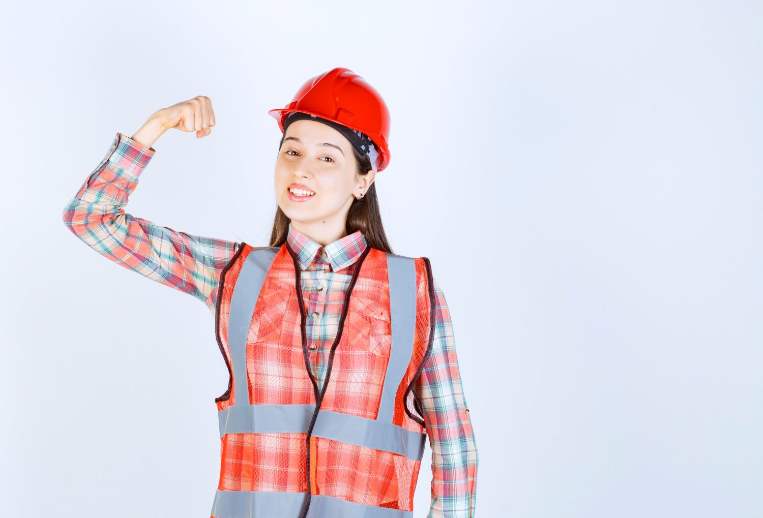 A woman wearing a hard hat and safety vest is flexing her muscles.