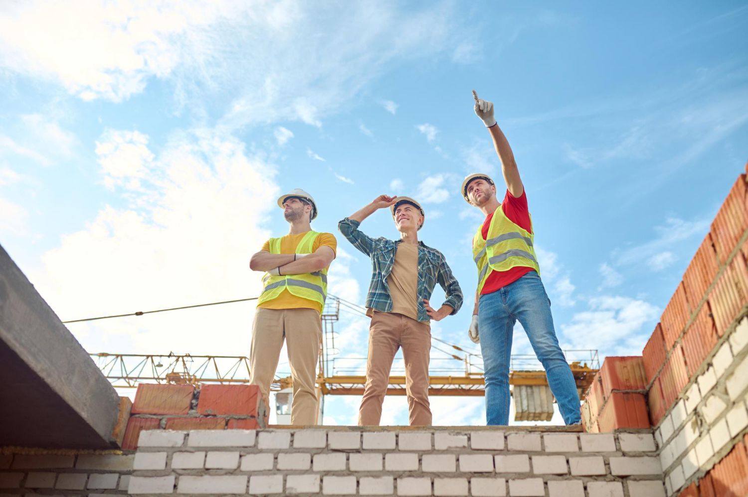 A group of construction workers are standing on top of a brick wall.