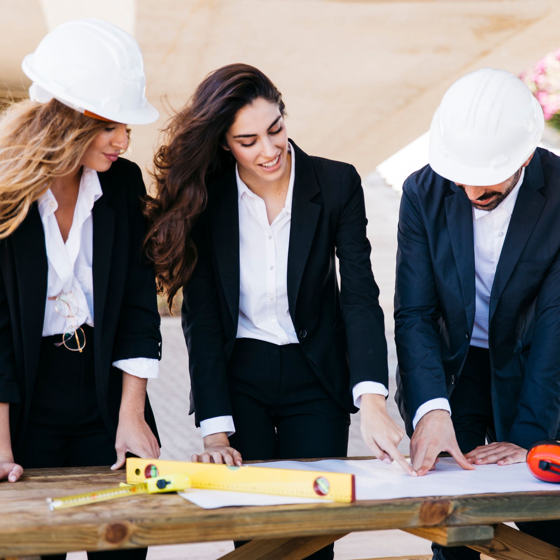 Three people wearing hard hats are looking at a blueprint