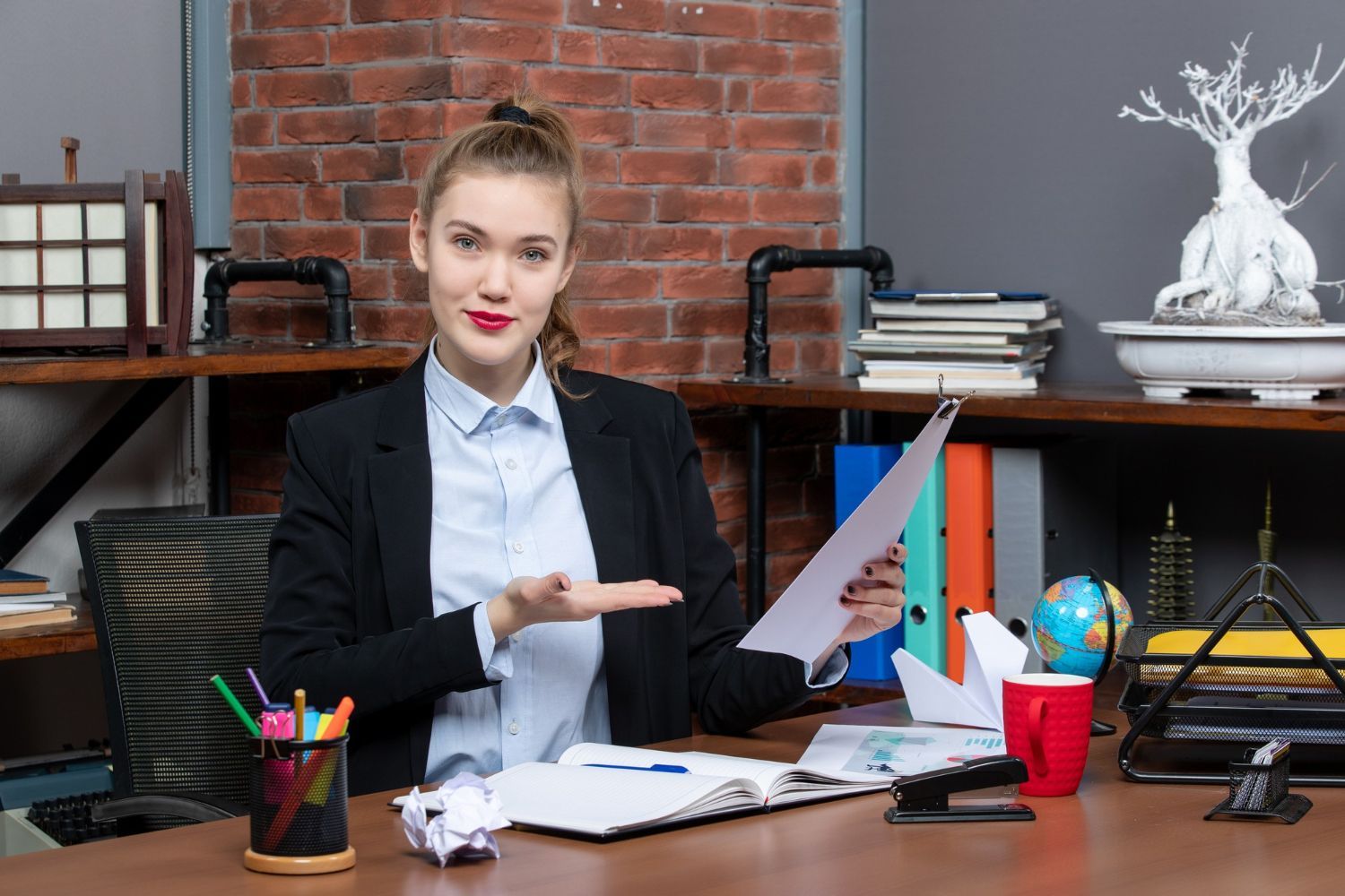 A woman is sitting at a desk in an office holding a piece of paper.