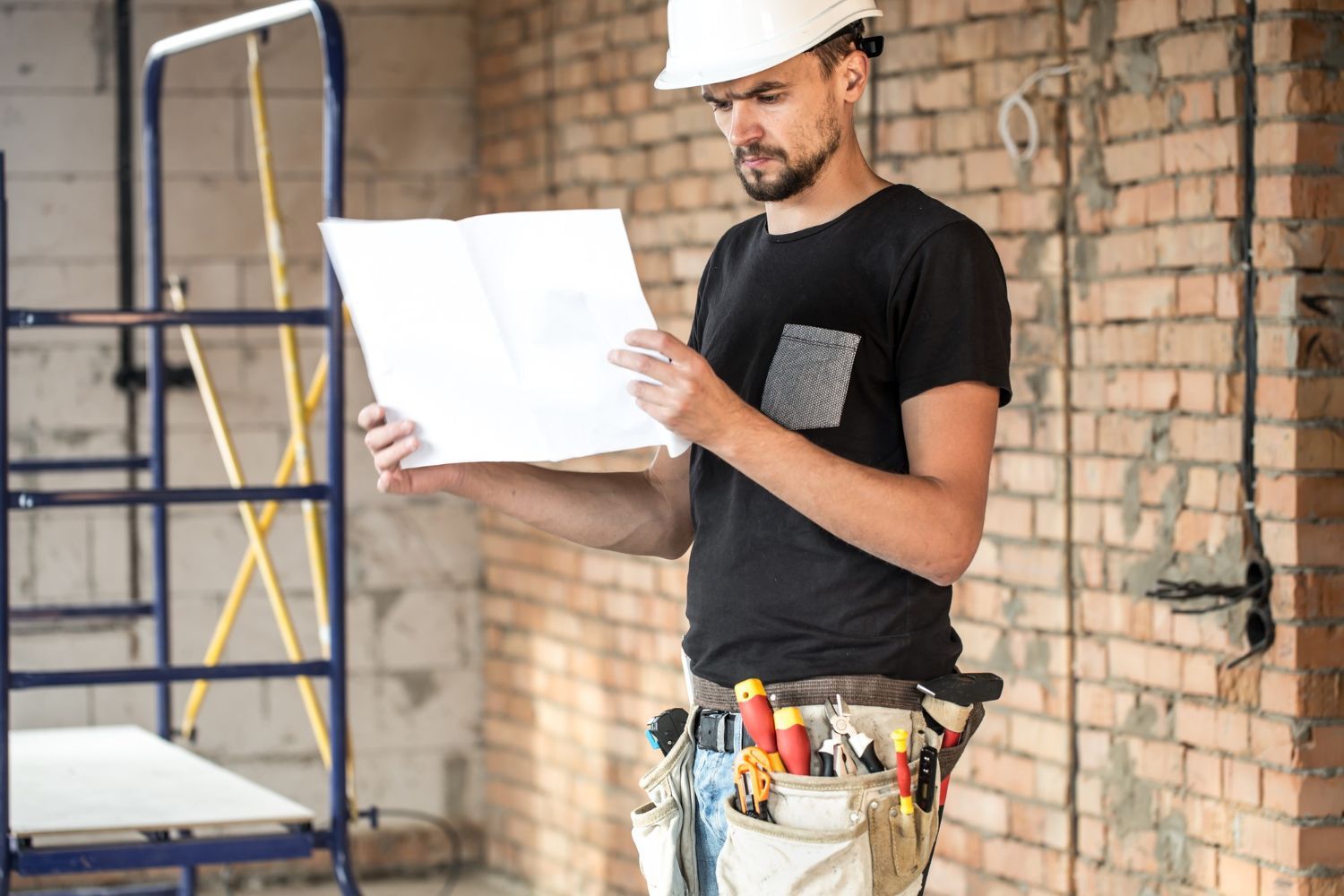 A man is standing in front of a brick wall looking at a blueprint.