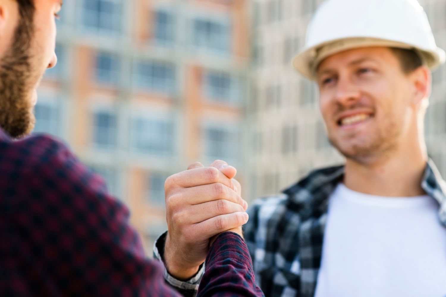 Two construction workers are shaking hands on a construction site.