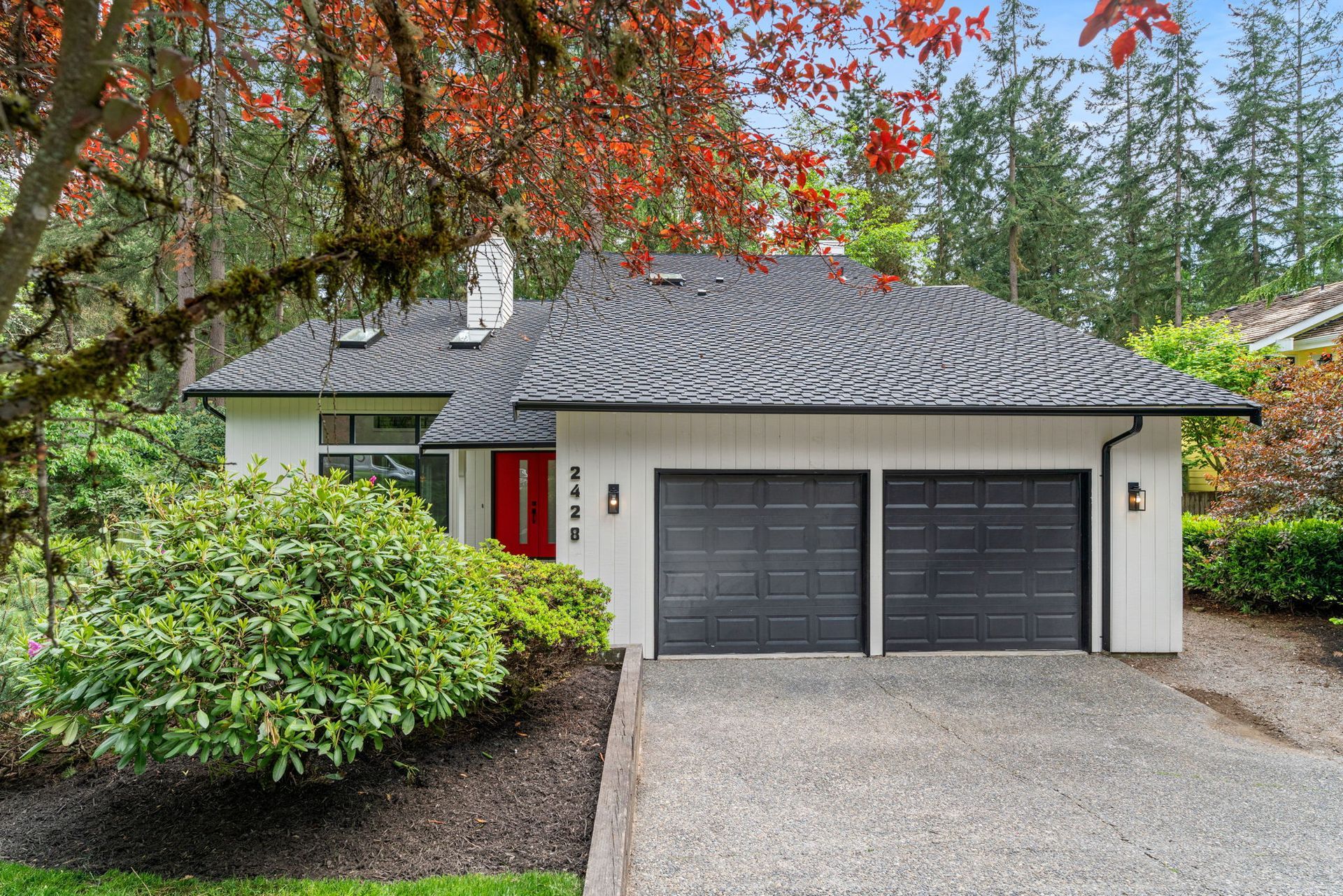 A white house with a black garage door and a red door.