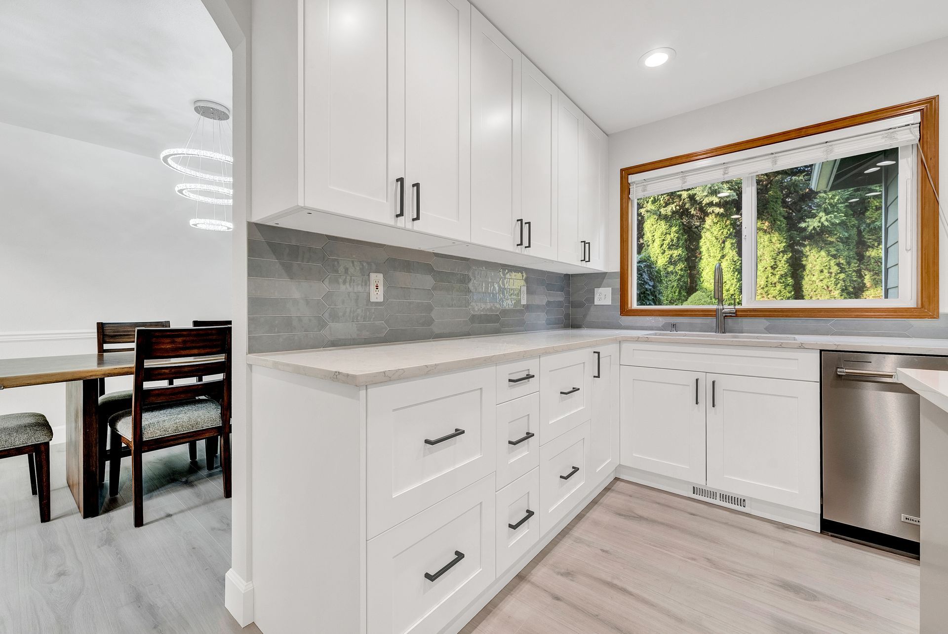 A kitchen with white cabinets , stainless steel appliances and a large window.