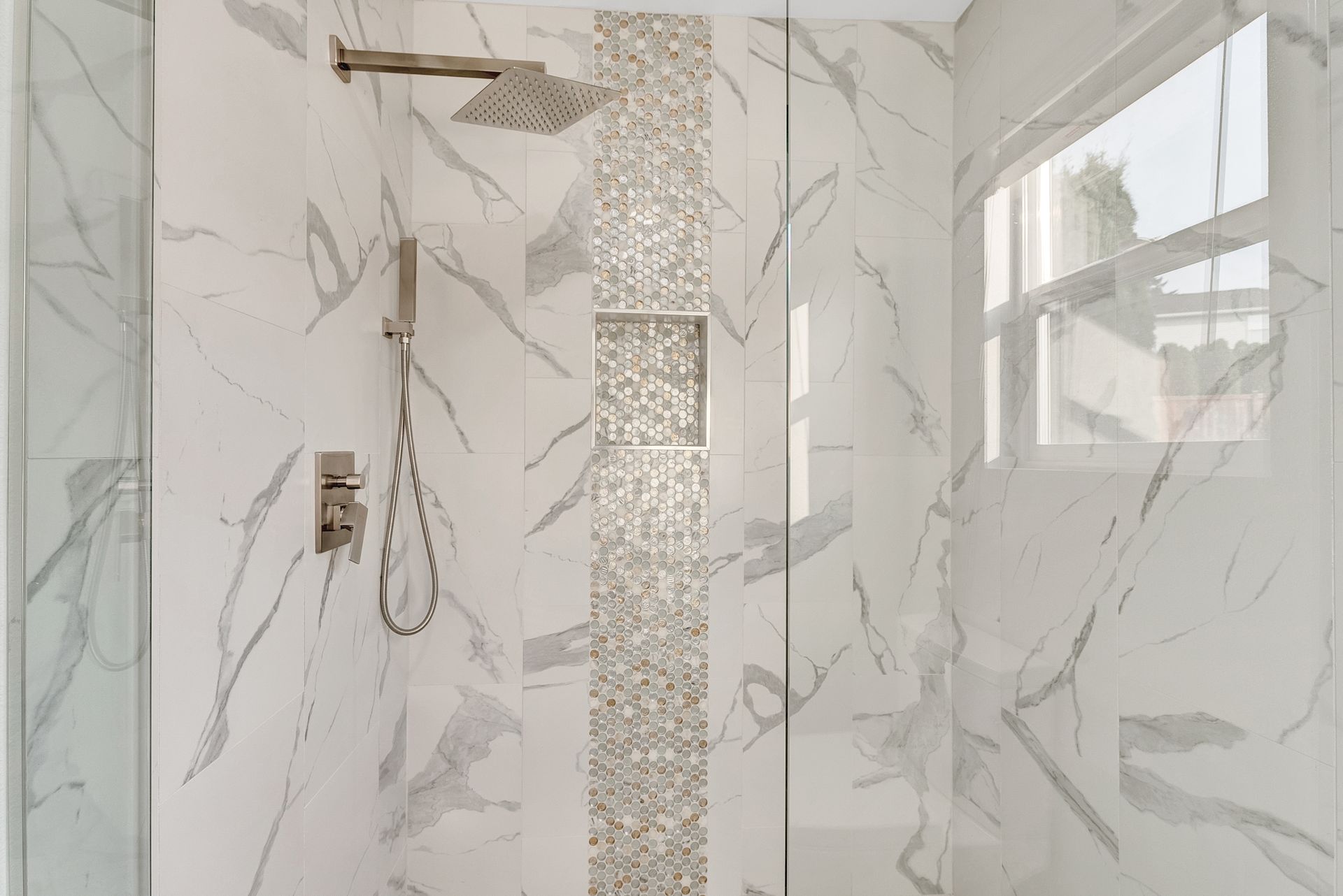 A bathroom with marble tiles and a walk in shower with a glass door.