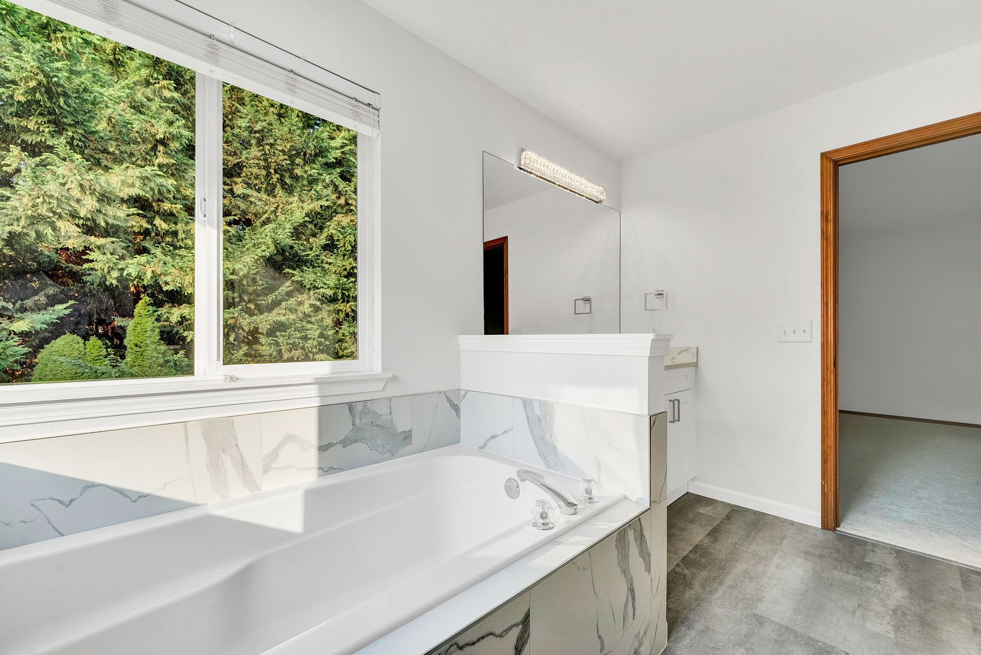 A bathroom with a tub , sink , mirror and window.