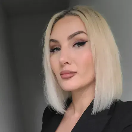 A woman with blonde hair is wearing a black jacket and looking at the camera.