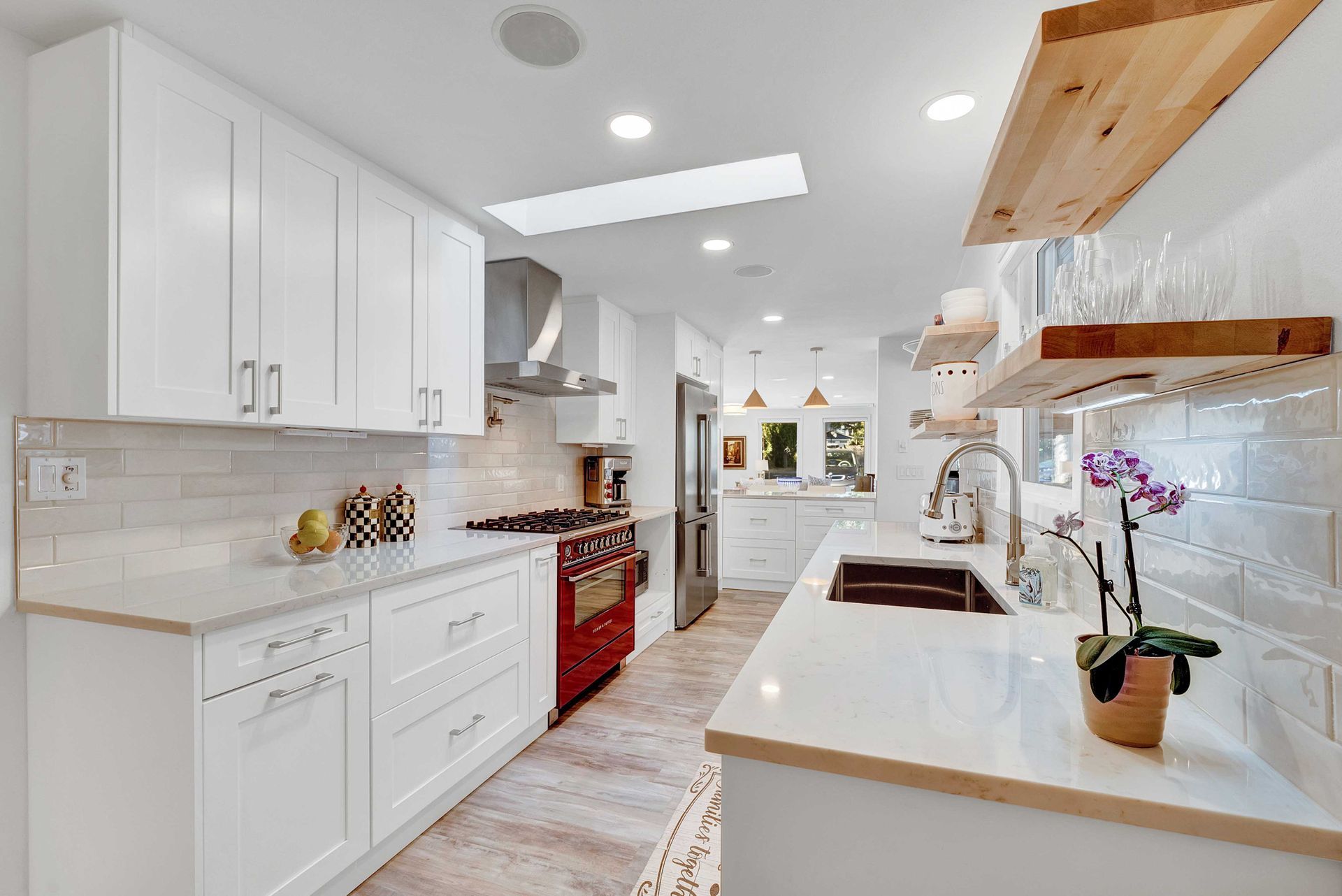 A kitchen with white cabinets , a red stove , a sink , and wooden shelves.