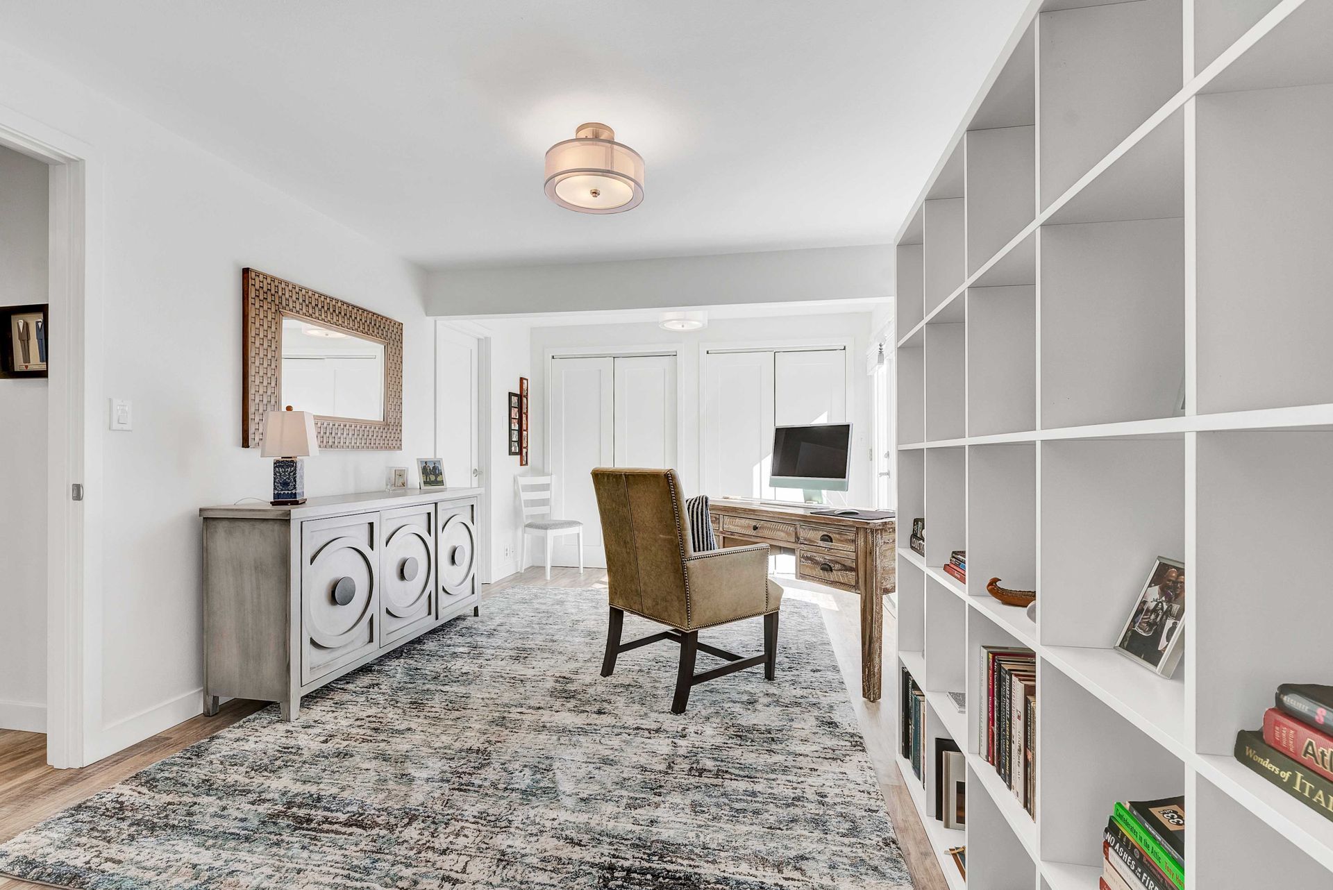 A living room with a rug , chair , desk and shelves.