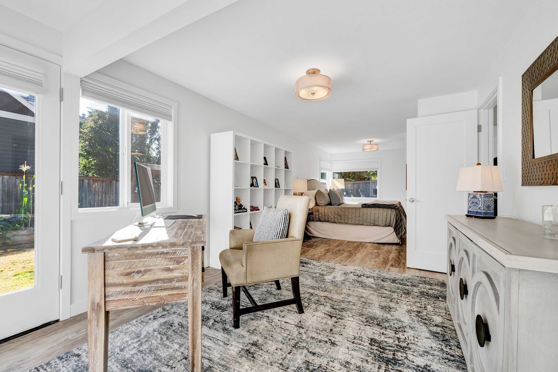 A living room with a desk , chair , rug and a large window.