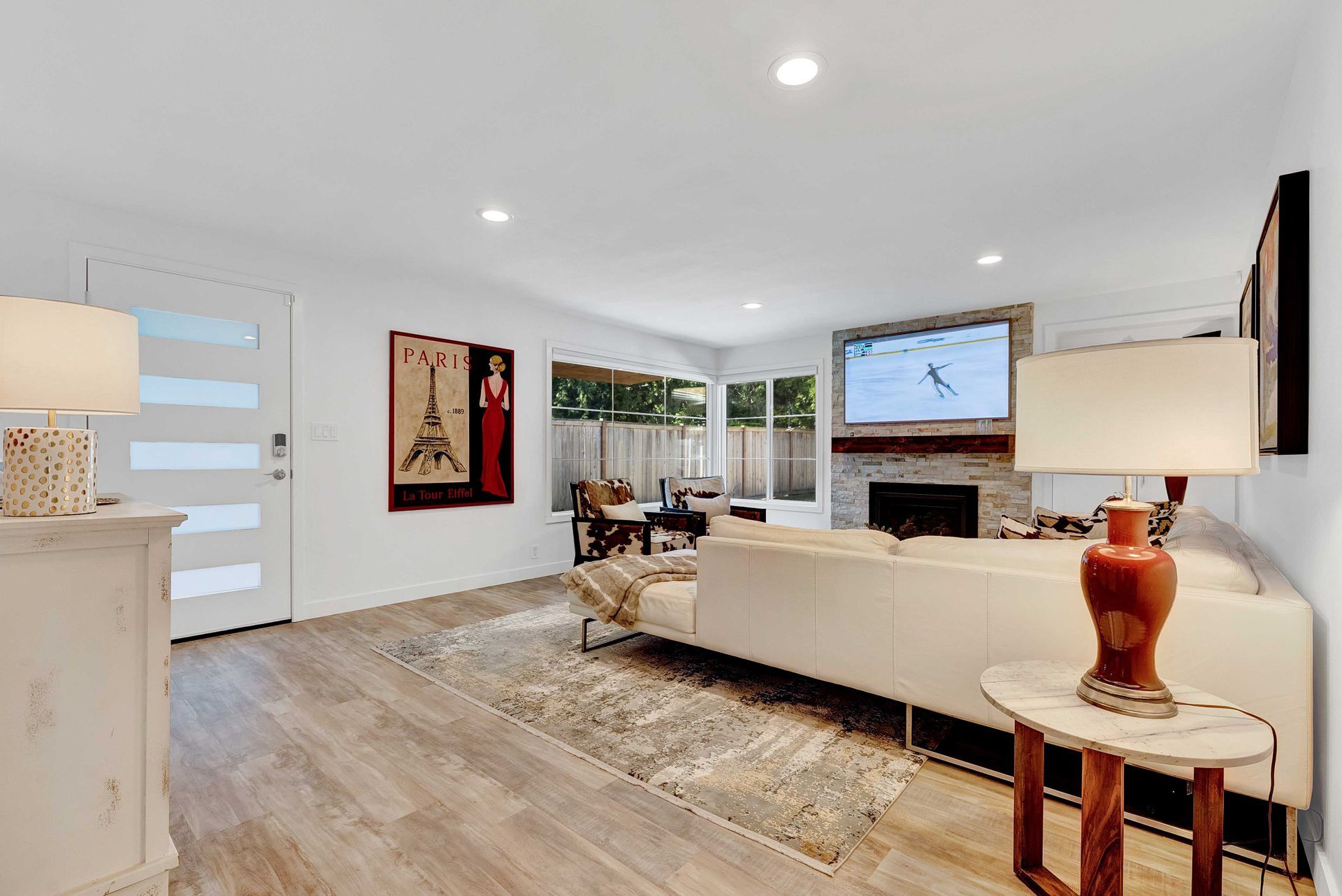 A living room with a white couch , lamps , a fireplace and a flat screen tv.