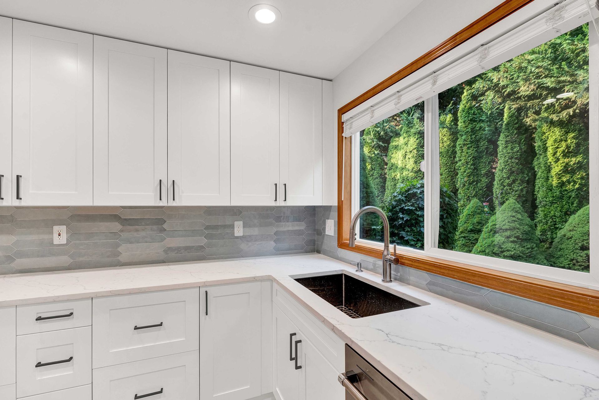 A kitchen with white cabinets , a sink , and a large window.