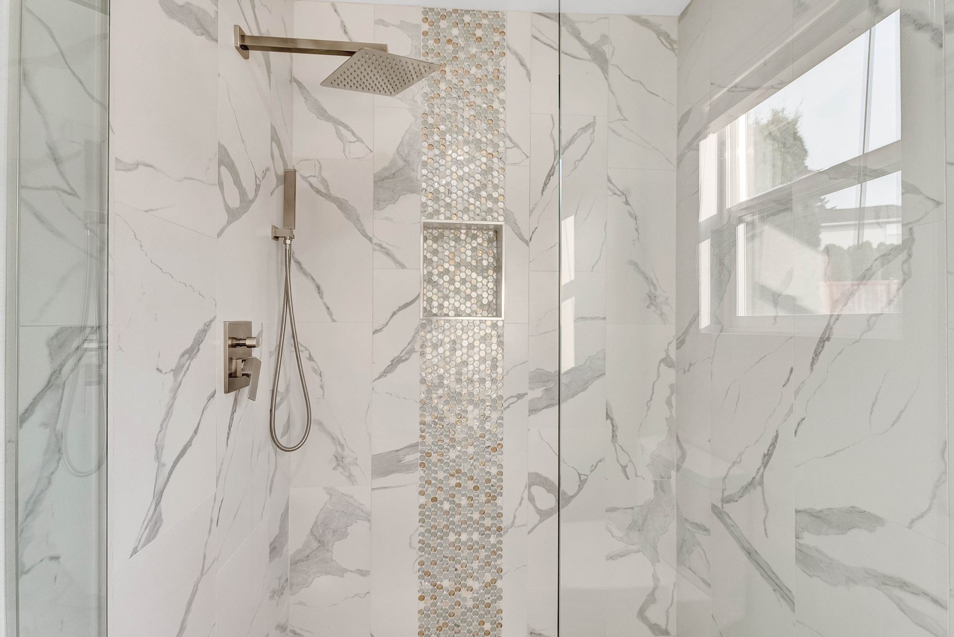 A bathroom with marble tiles and a walk in shower with a glass door.