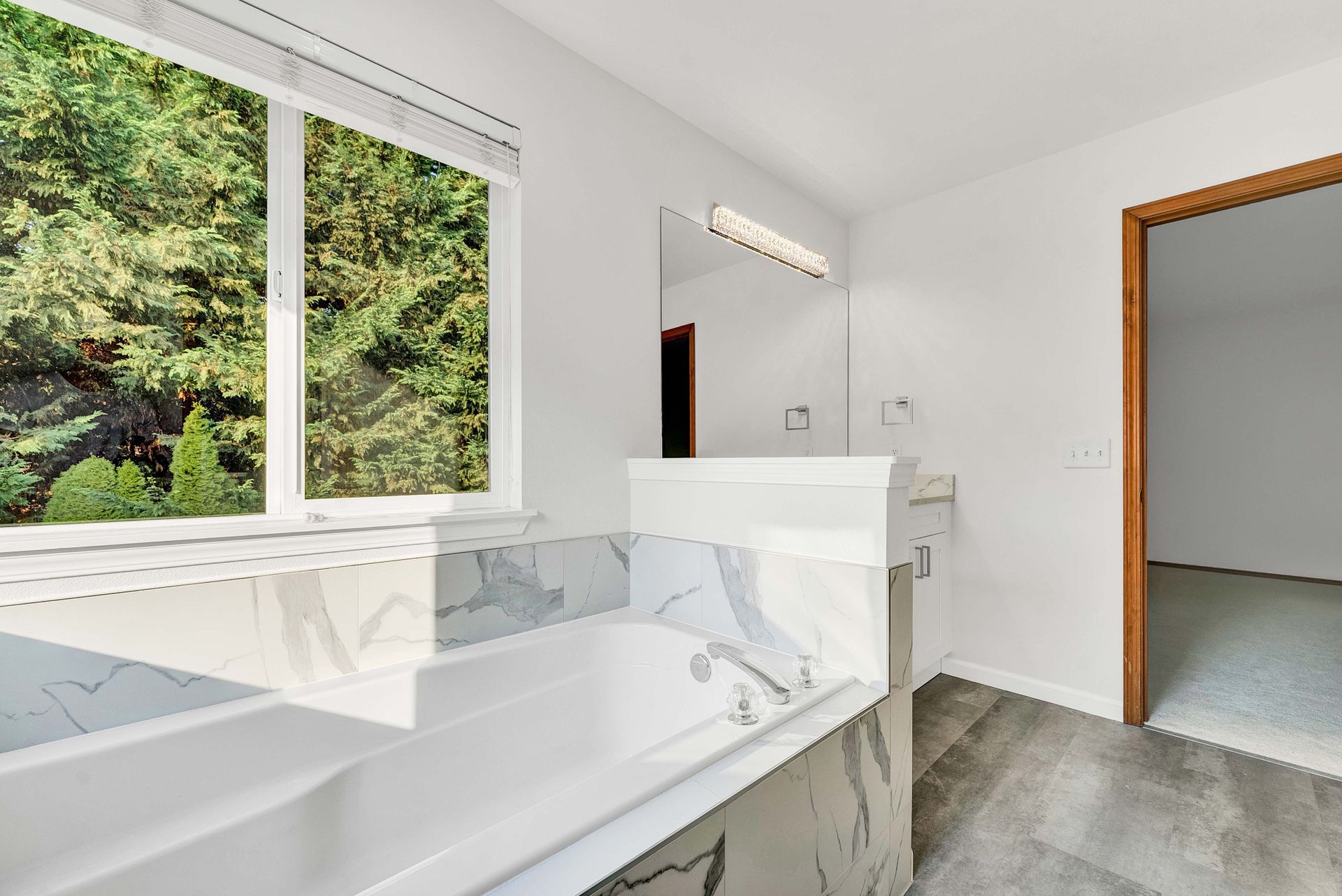 A bathroom with a tub , sink , mirror and window.