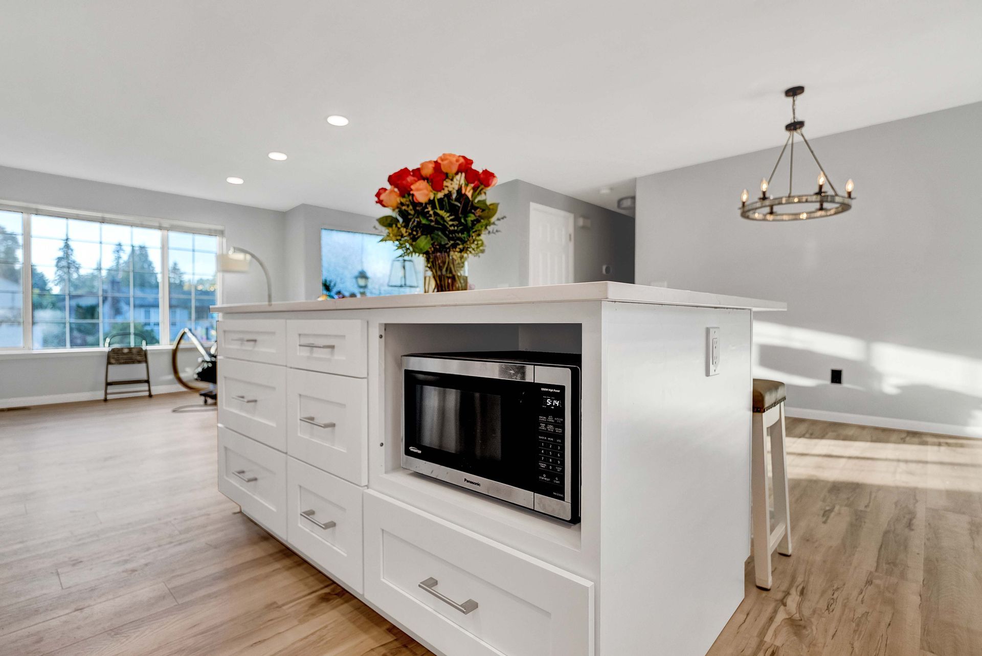 A kitchen with a microwave and a vase of flowers on the island.