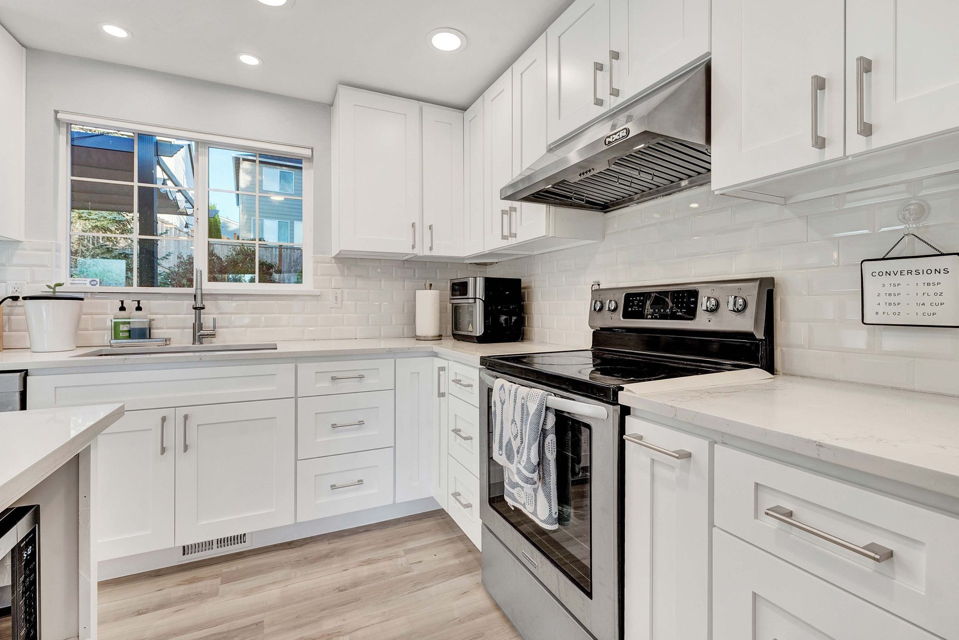 A kitchen with white cabinets , a stove , a sink , and a window.