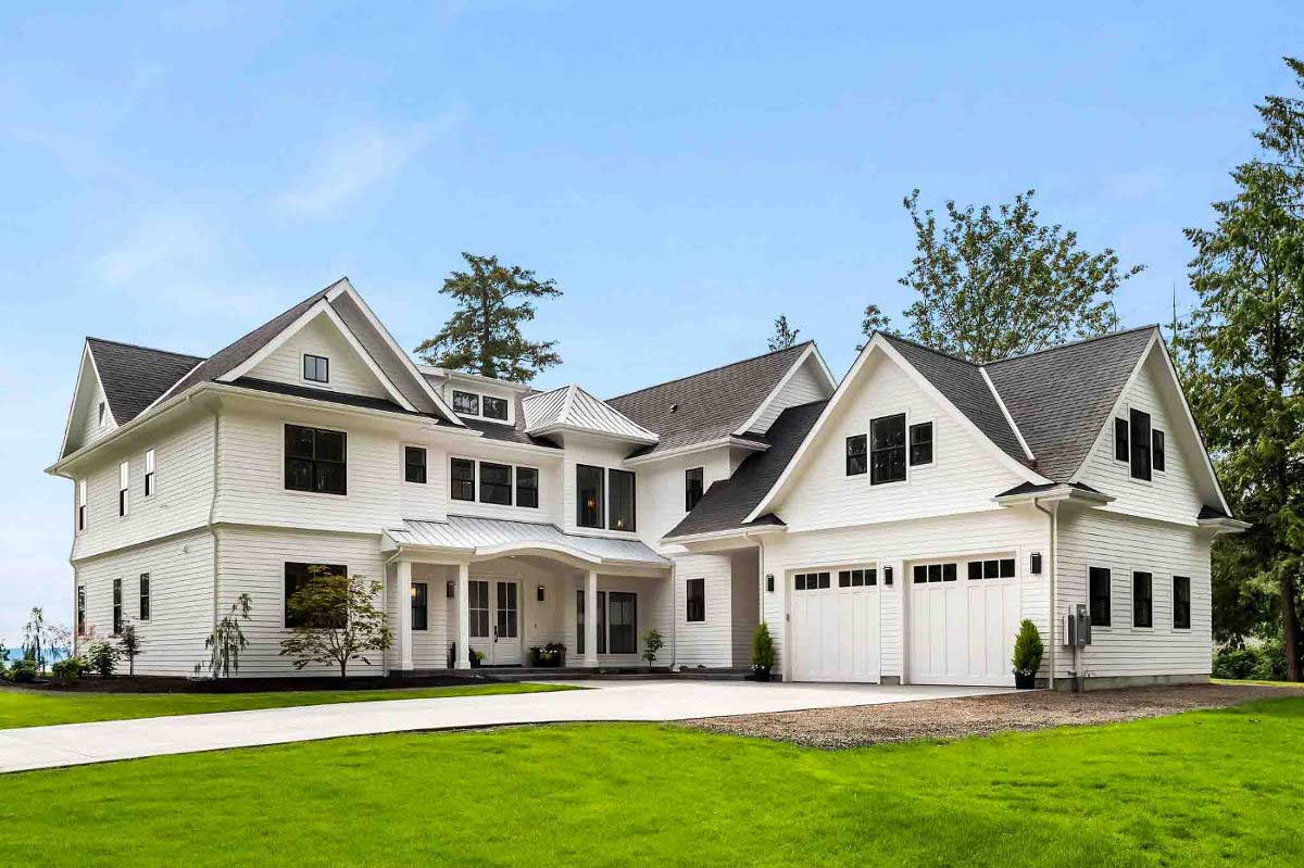 A large white house with a black roof is sitting on top of a lush green field.