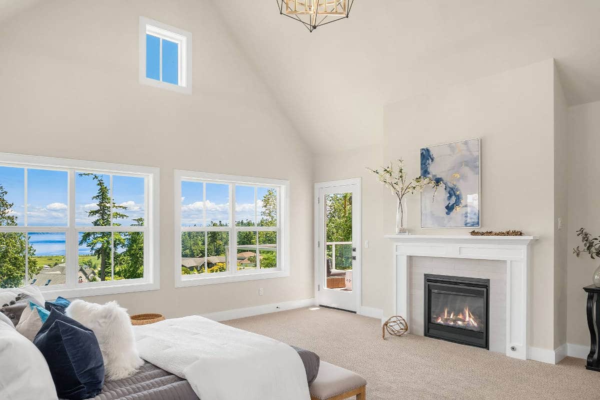 A bedroom with a bed , fireplace , and lots of windows.