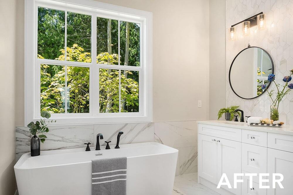 A bathroom with a tub , sink , mirror and window.