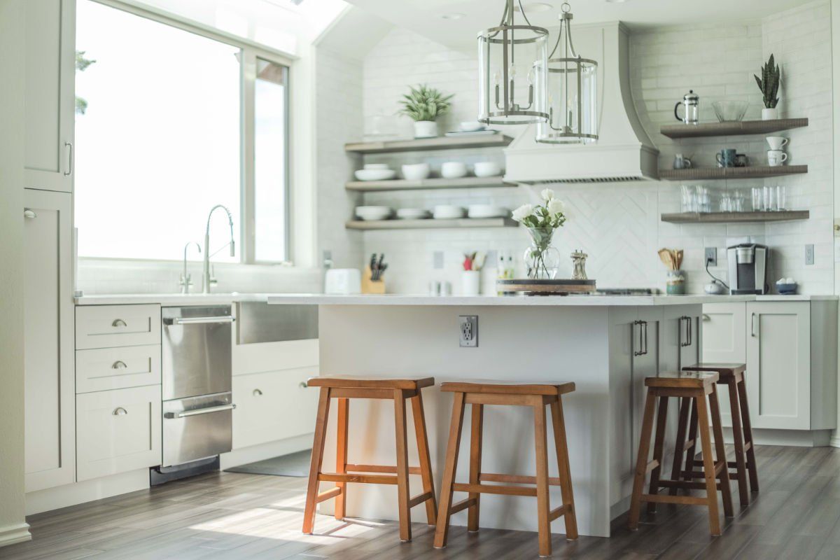 A kitchen with white cabinets , stainless steel appliances , and wooden stools.