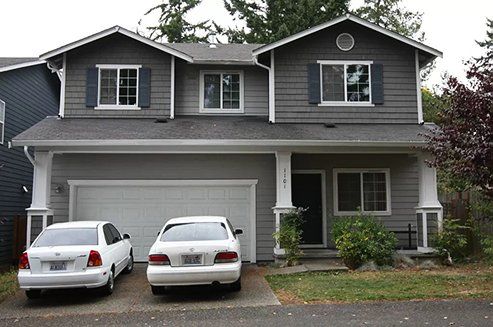 Two cars are parked in front of a large house