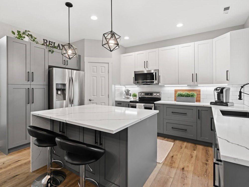 A kitchen with gray cabinets , white counter tops , stainless steel appliances and a large island.