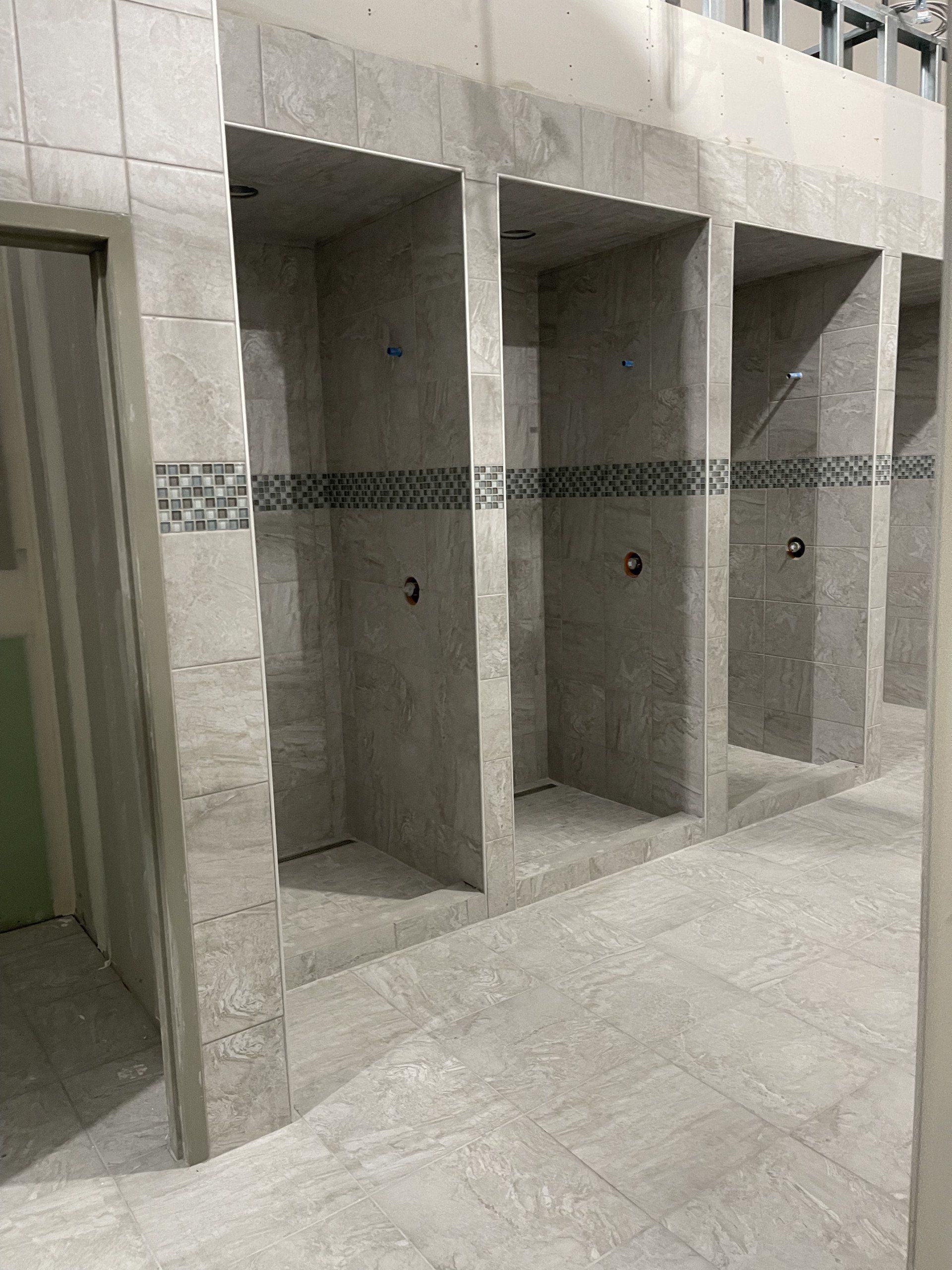 A bathroom with a row of shower stalls lined up next to each other.