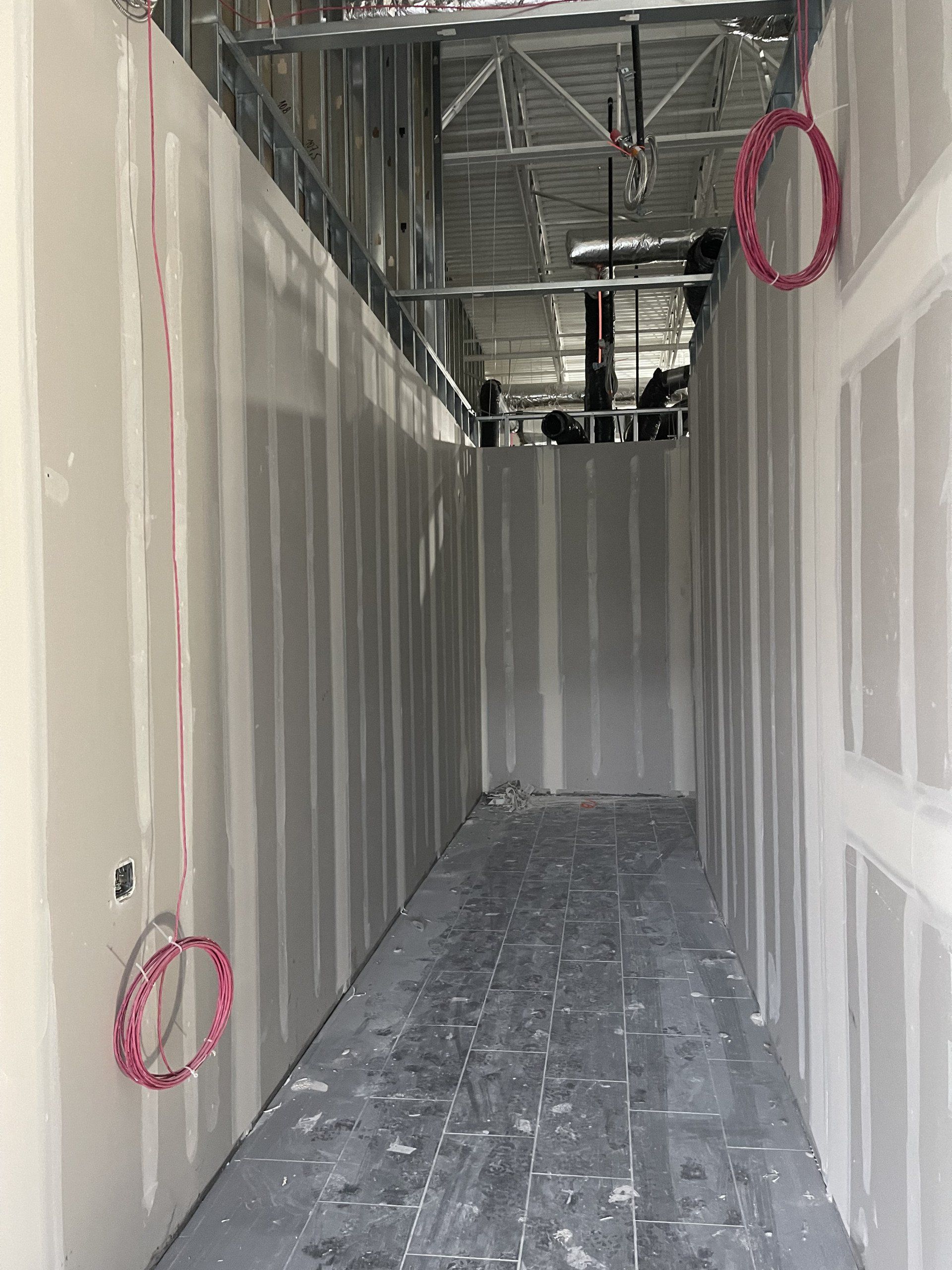 A long hallway with drywall walls and electrical wires hanging from the ceiling.