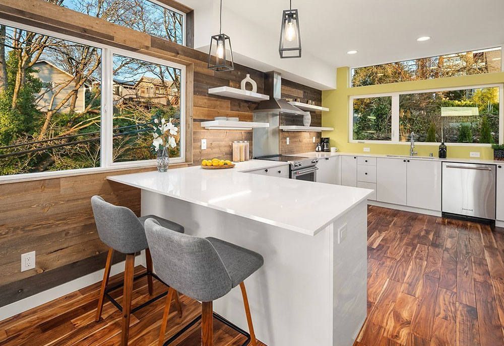 A kitchen with a large island , wooden floors , white cabinets and stools.