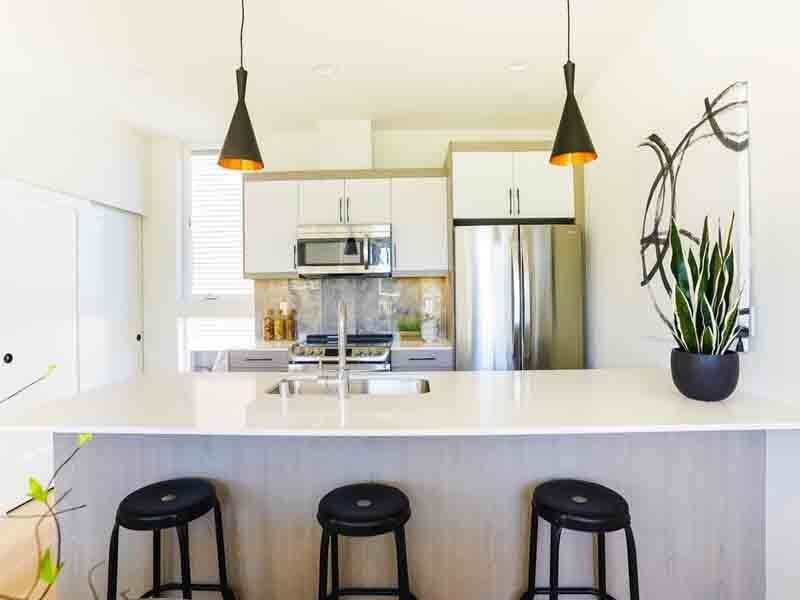 A kitchen with stools , a sink , a refrigerator and a microwave.